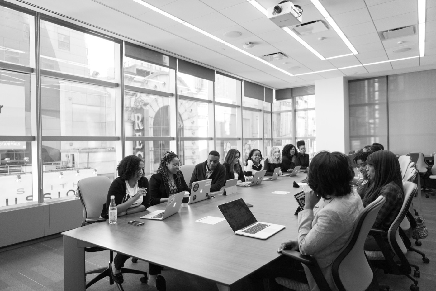 A cohort with laptops around a long table in a bright office.