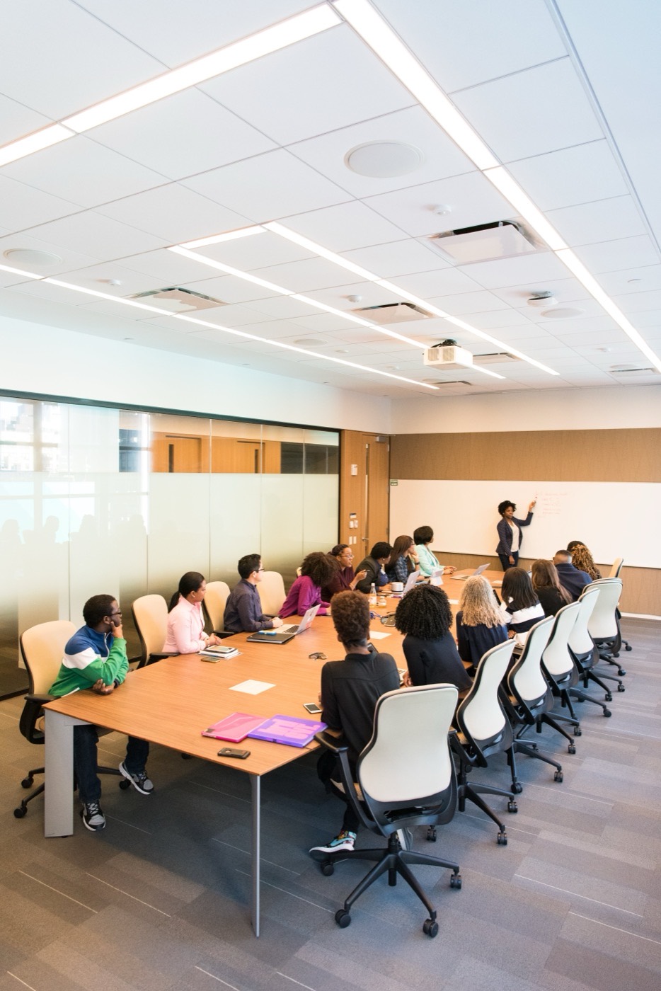 An instructor at a whiteboard with a cohort around a conference table and laptops.