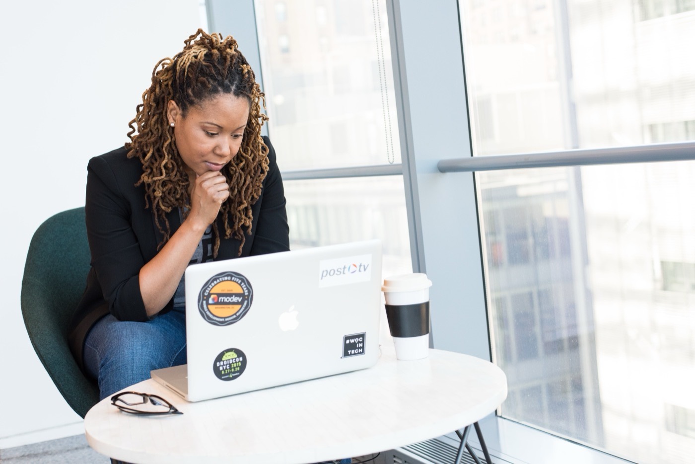 Instructor with locs and a blazer working on a laptop.
