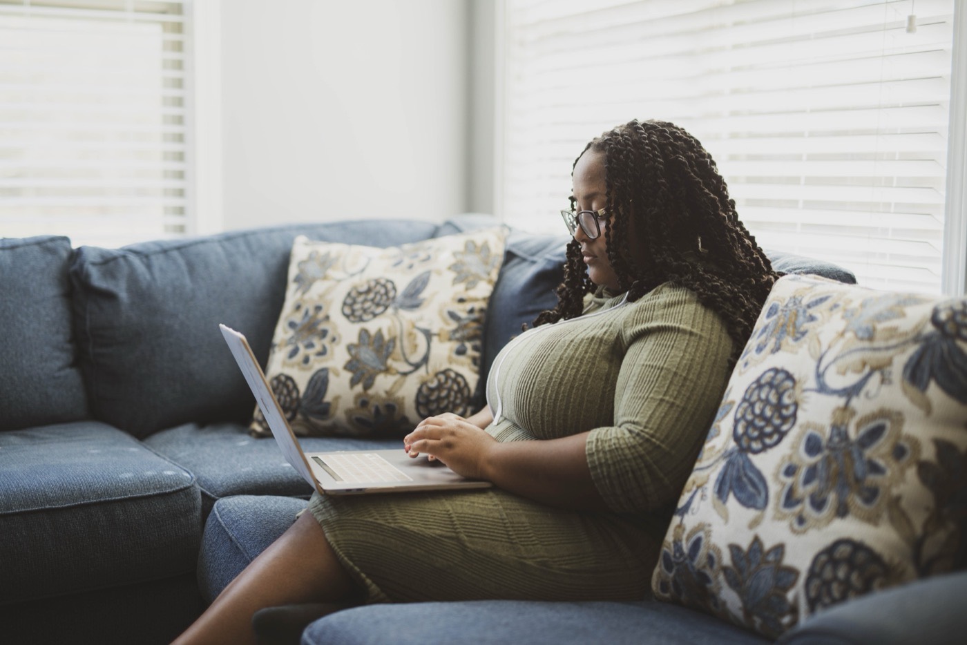 Learner with braids and glasses working from a home sofa.